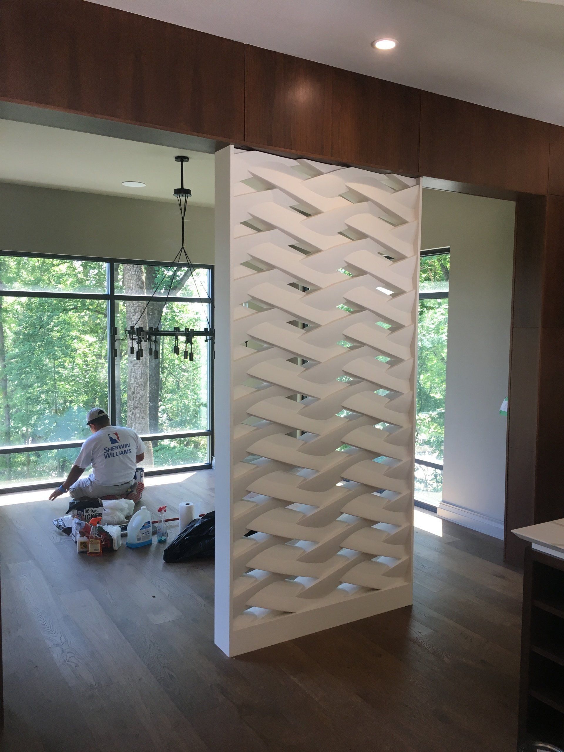 Modern living room with a white lattice partition and a person sitting near windows, with tools on the floor