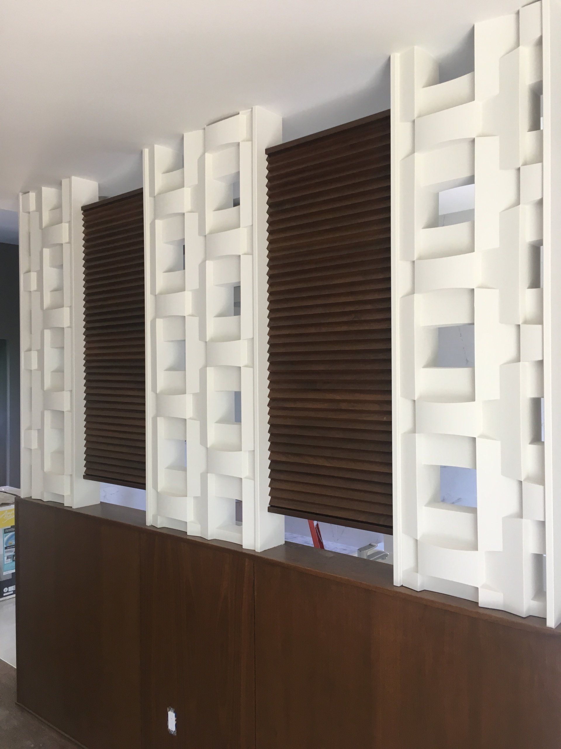 Modern interior with white geometric wall panels, dark blinds, and wood wainscoting along a wall