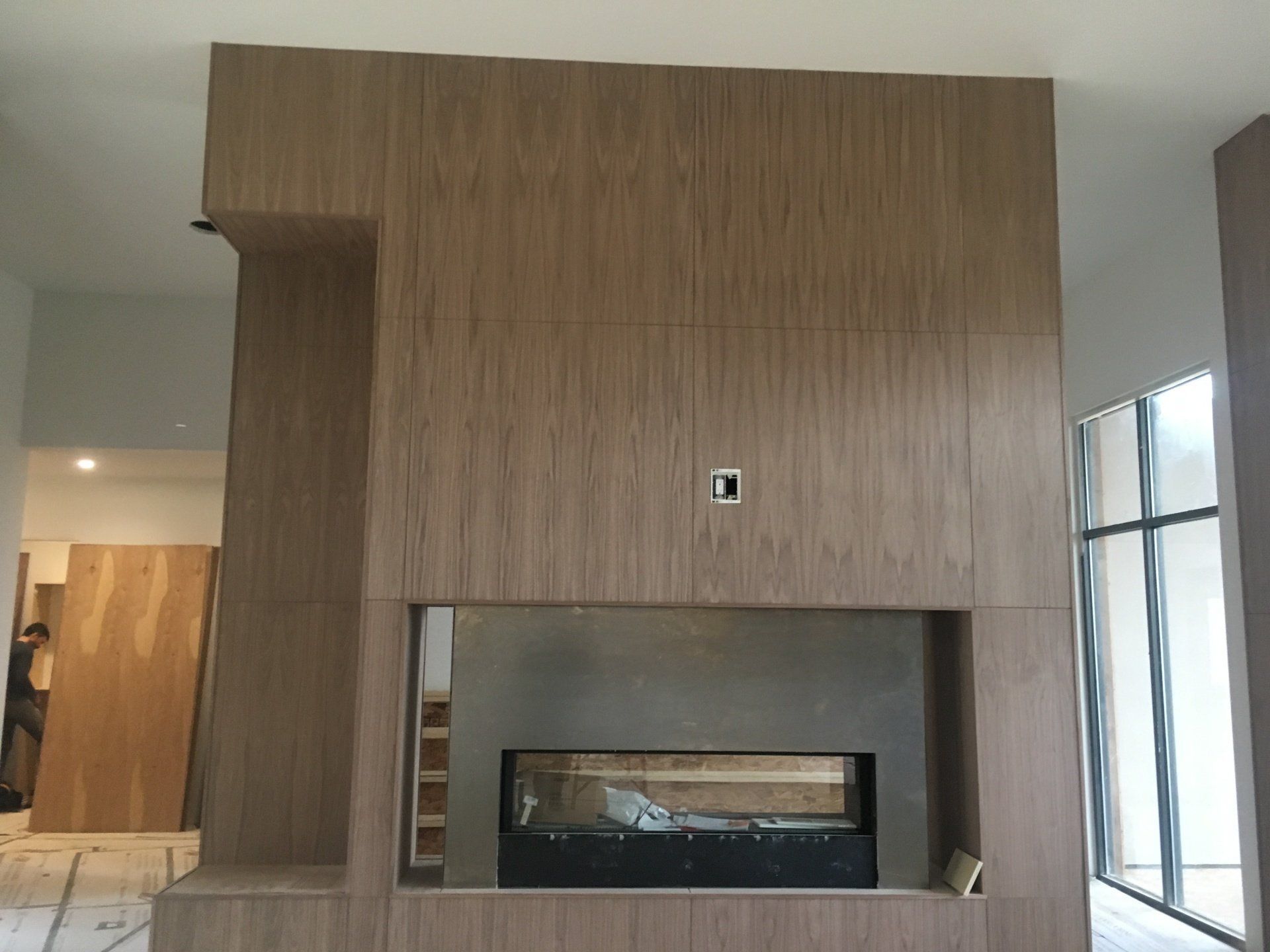 Modern interior with a large wood-paneled fireplace wall and built-in fireplace under a window.