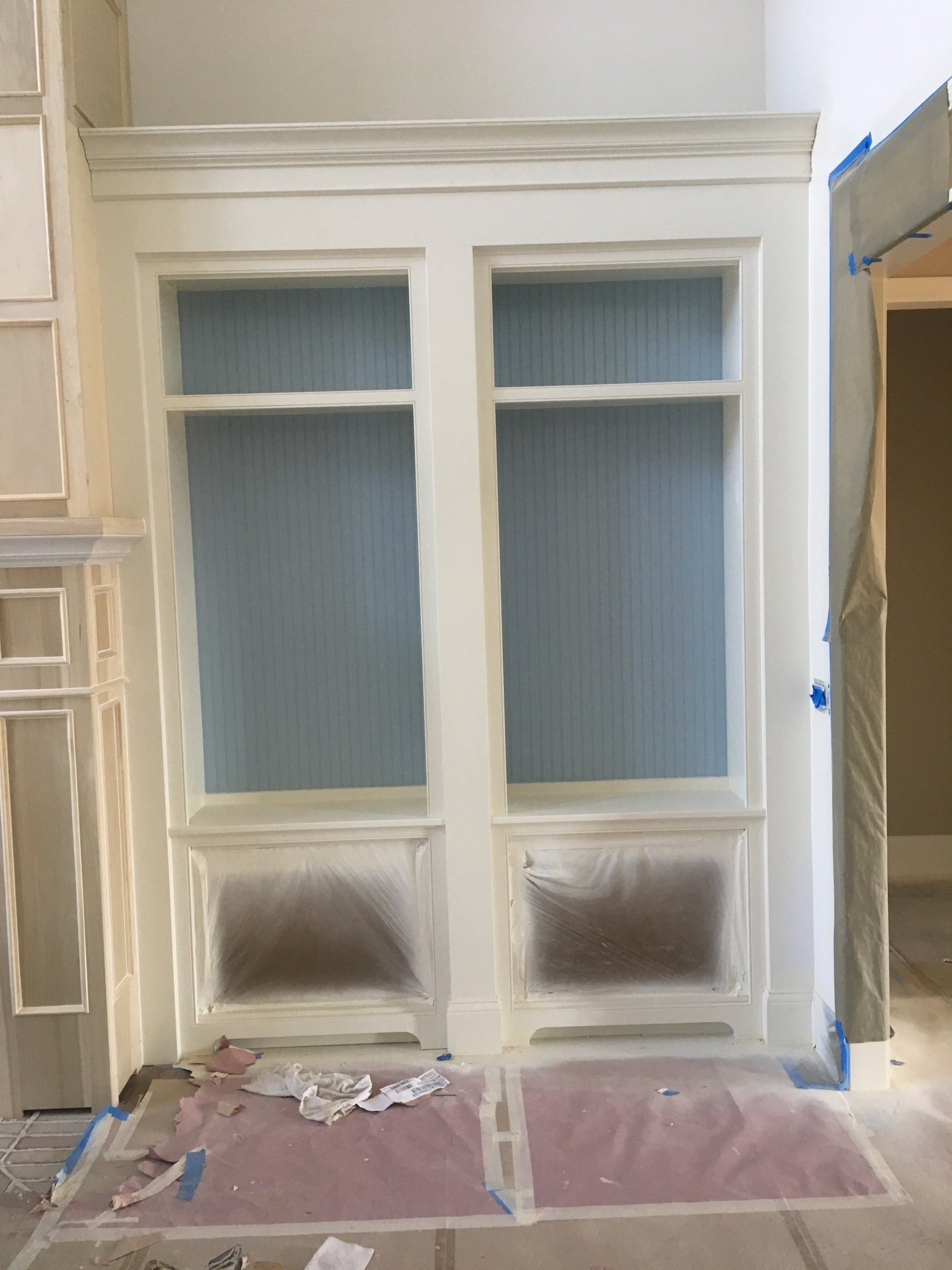 White built-in cabinets or window panels under renovation, covered with masking paper and drop cloths.