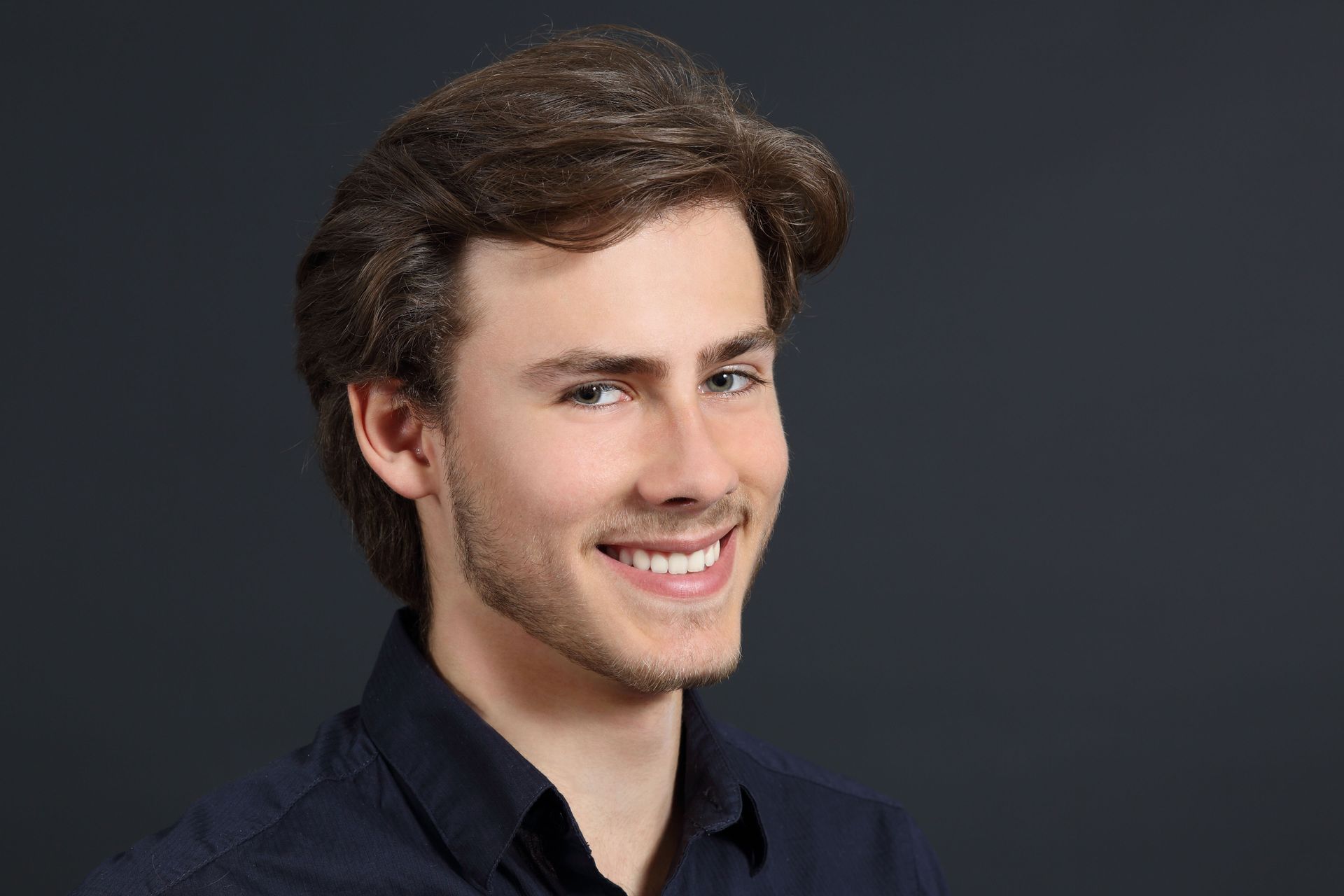 A young man with a beard is smiling and wearing a black shirt.