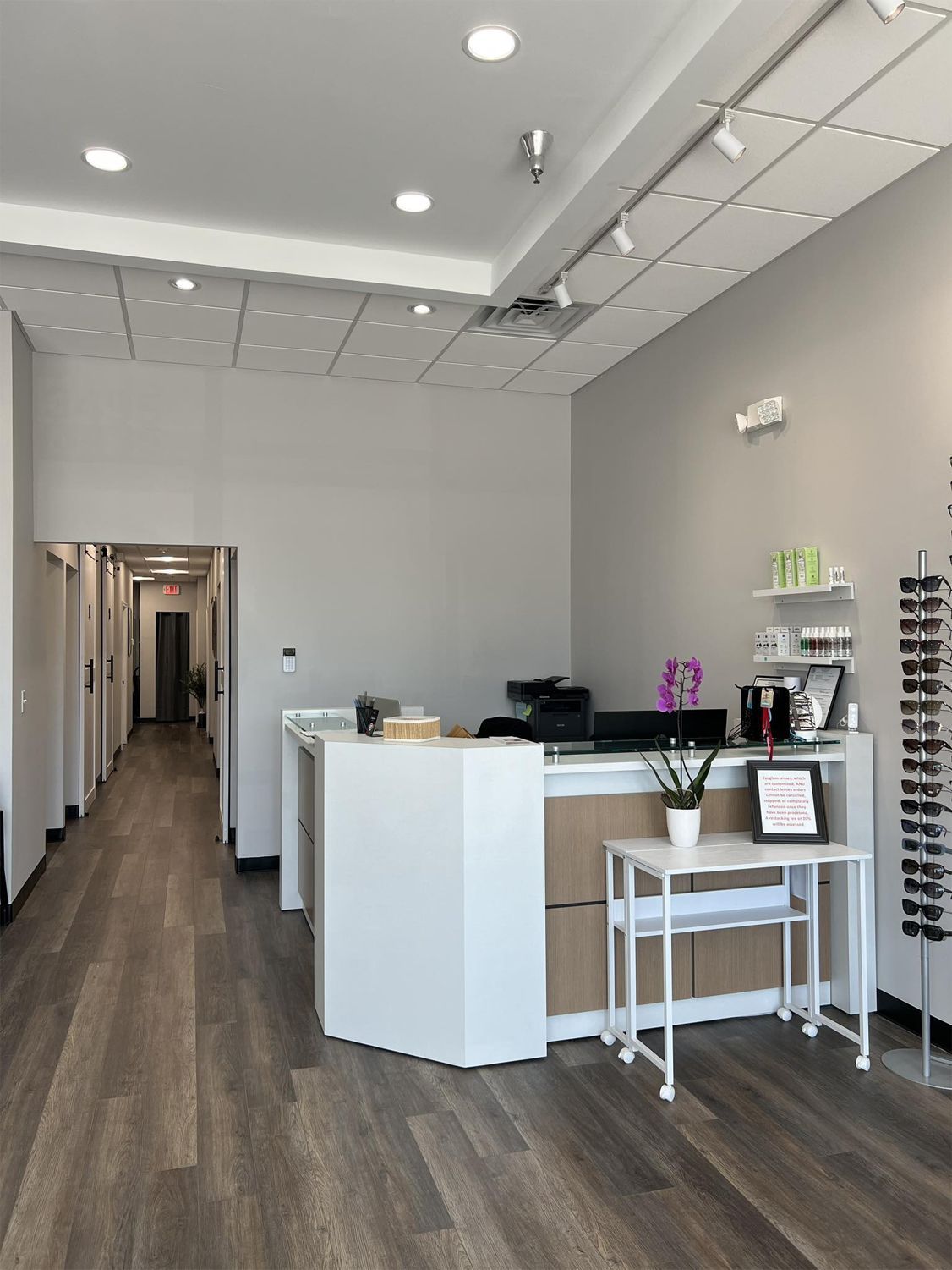Reception area of a clinic with a white desk, gray walls, and a long hallway leading to examination rooms.