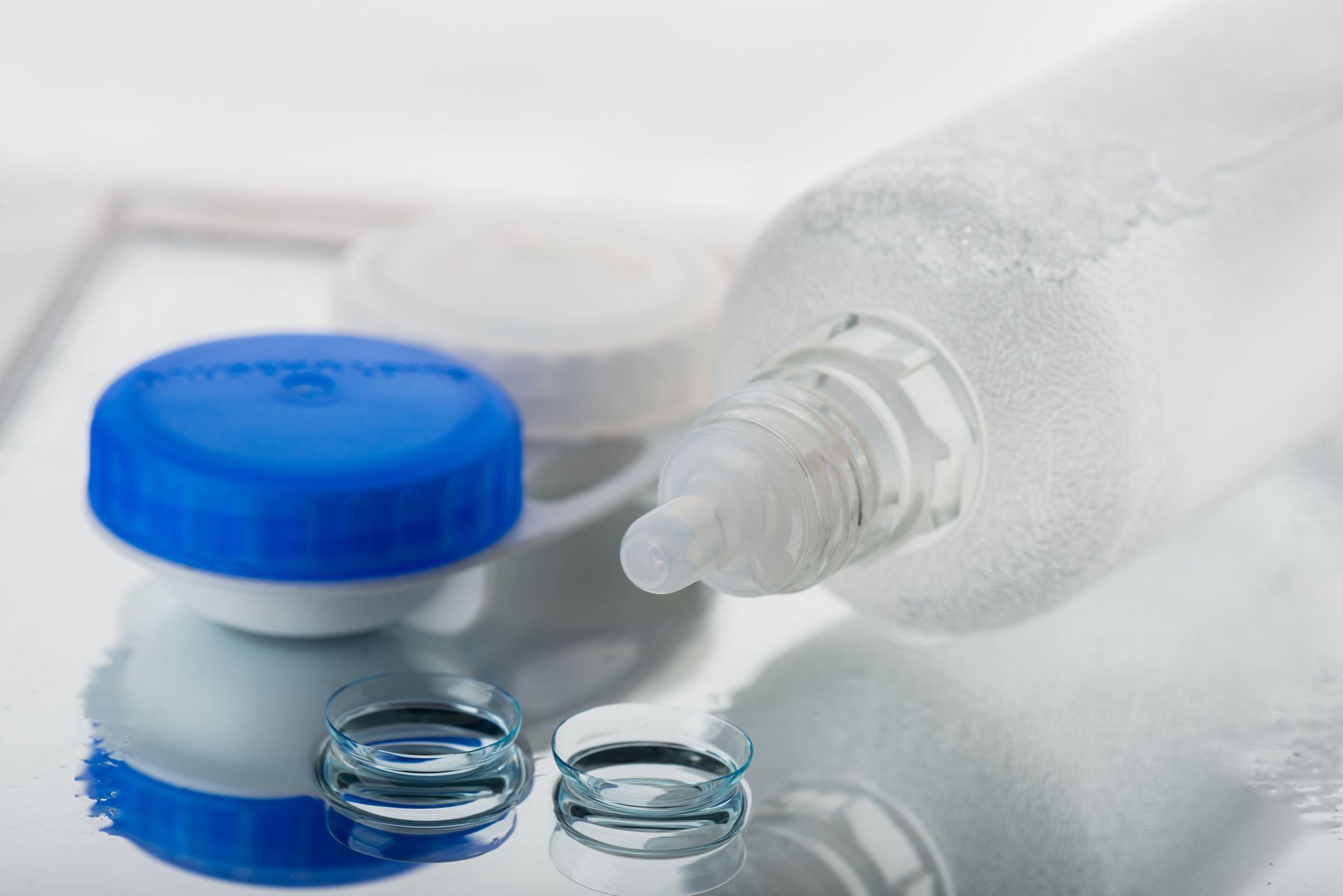 Contact lenses with solution bottle and case on a reflective surface. Blue and white colors.