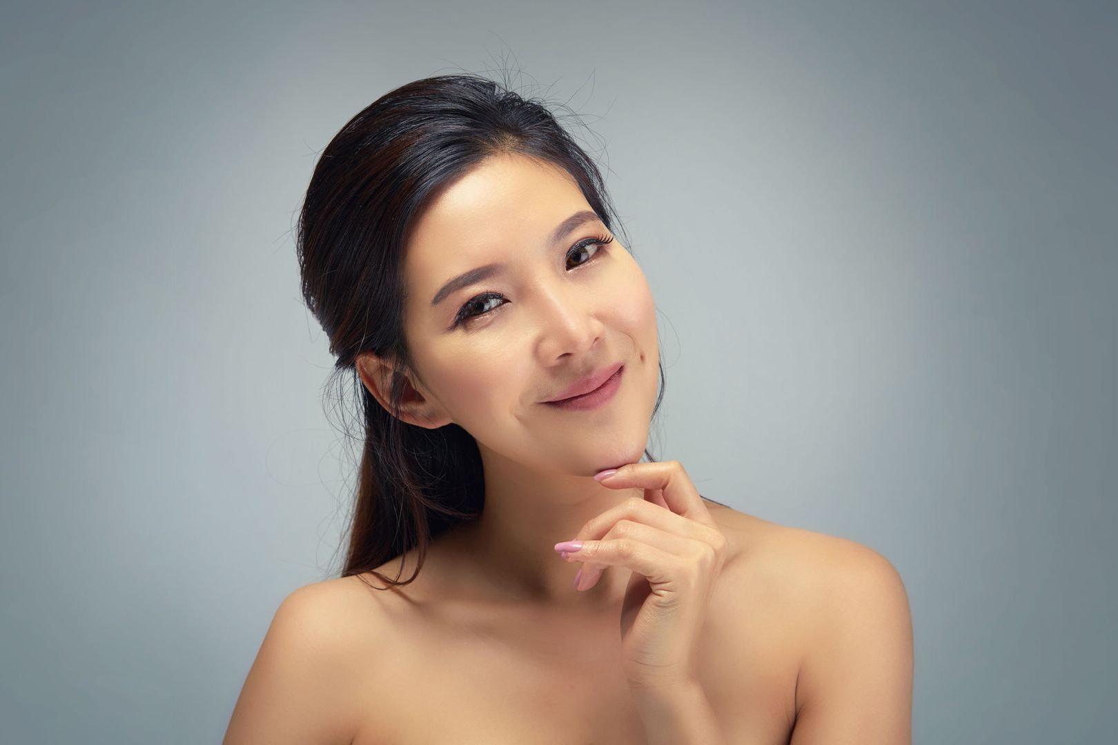 A woman without a shirt is smiling with her hand on her chin.