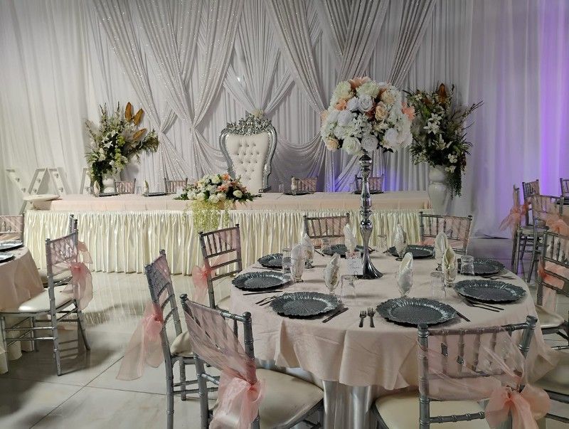 Wedding reception with a decorated head table, round guest table, and floral arrangements.