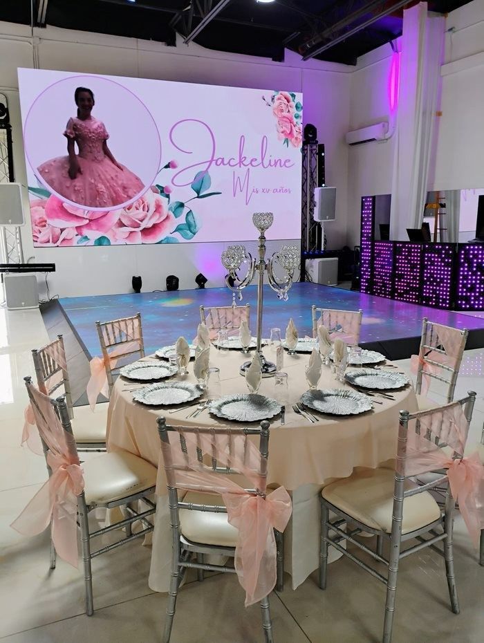 Table set for an event, pink theme. A screen shows a girl in a pink dress, the background is a ballroom.