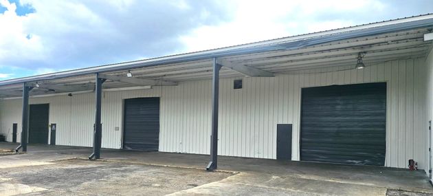 Row of white industrial warehouse units with black roll-up doors under a metal awning.