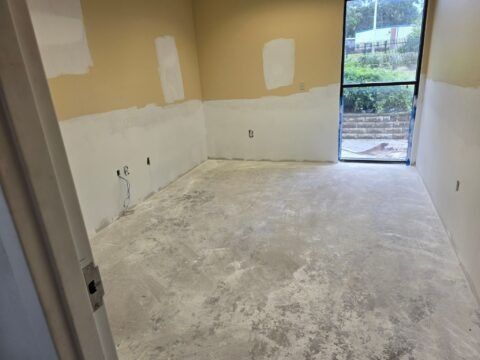 Empty room under renovation with bare concrete floor, unfinished walls, and a glass door to outside.