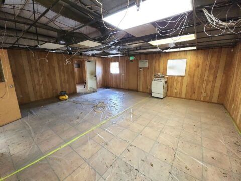 Empty unfinished basement with wood-paneled walls, exposed ceiling wires, and tiled floor under bright lights