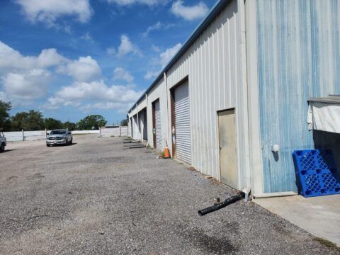 Gravel lot beside a blue-gray warehouse under a partly cloudy sky