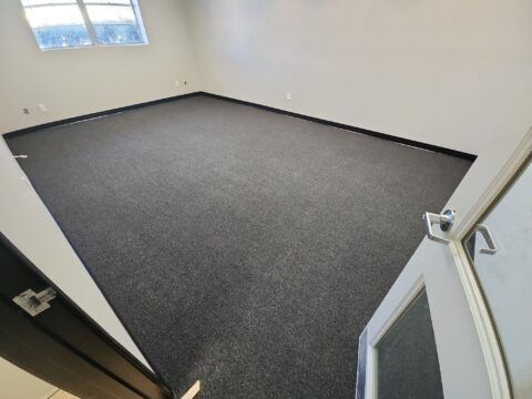 Empty carpeted room with white walls and a window, viewed from the doorway