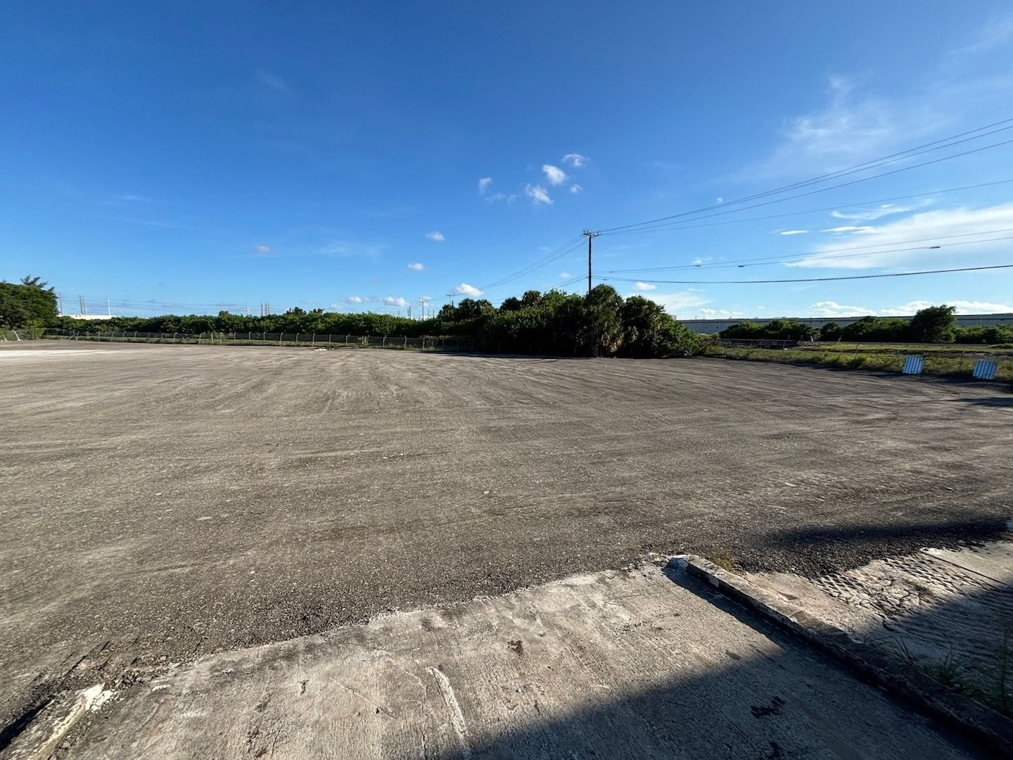 Empty gravel lot under a bright blue sky with a low tree line in the distance