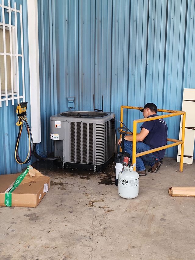 Man kneeling by yellow barrier next to propane tank and HVAC unit beside a blue wall.
