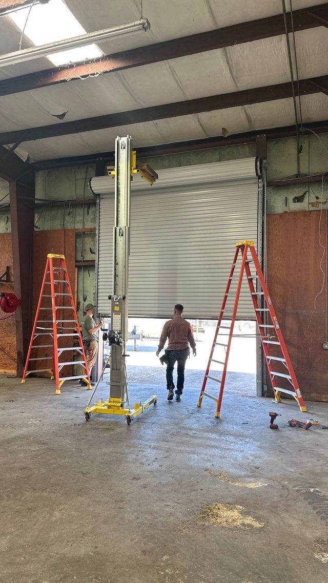 Warehouse with two red ladders and a person walking beside a tall yellow lift under a closed roll-up door