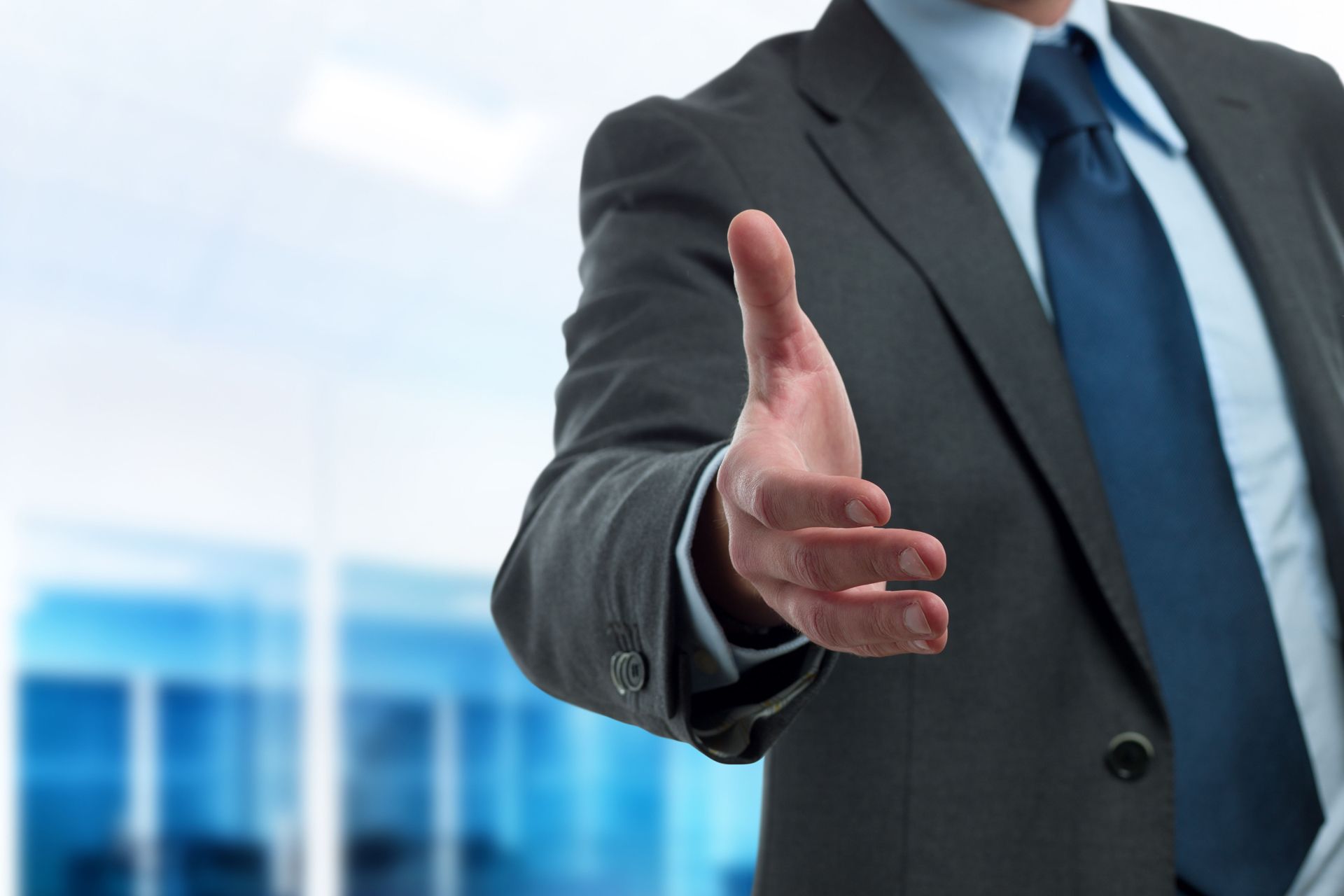Businessman in a dark suit extending a handshake in a modern office setting