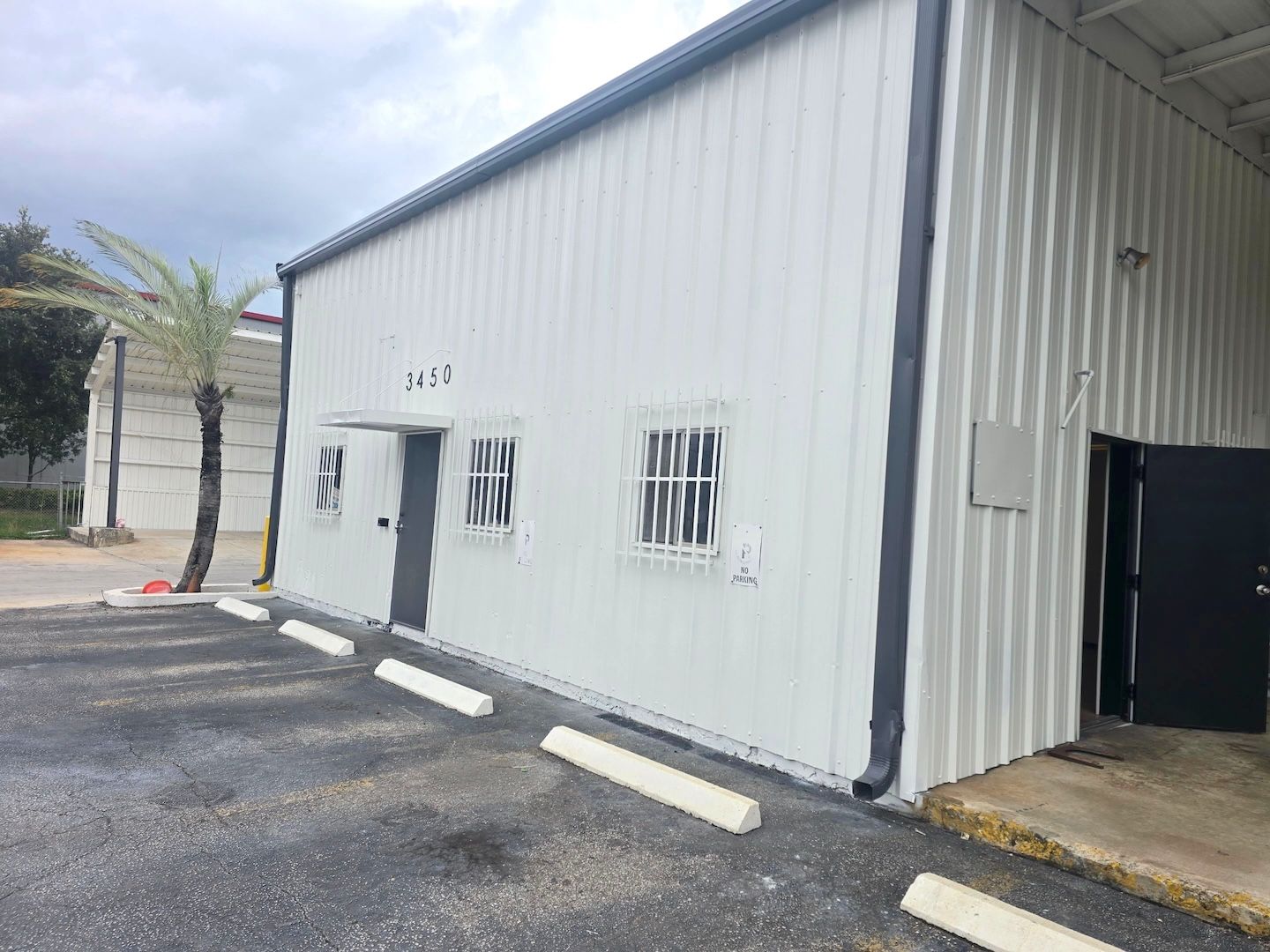 White corrugated metal building with small windows and a driveway beside it.
