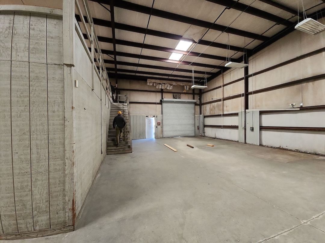 Empty industrial warehouse interior with concrete floor, metal walls, and overhead lights.