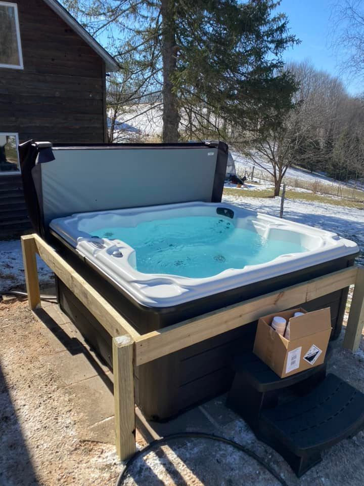 A hot tub is sitting in the snow in front of a house.