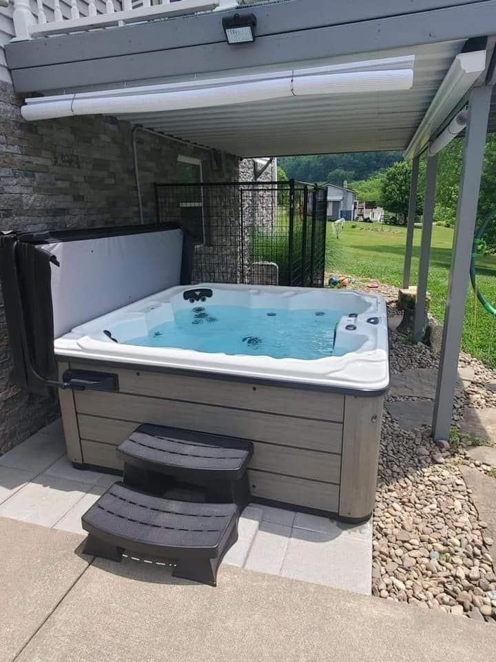 A hot tub is sitting under a canopy on the side of a house.