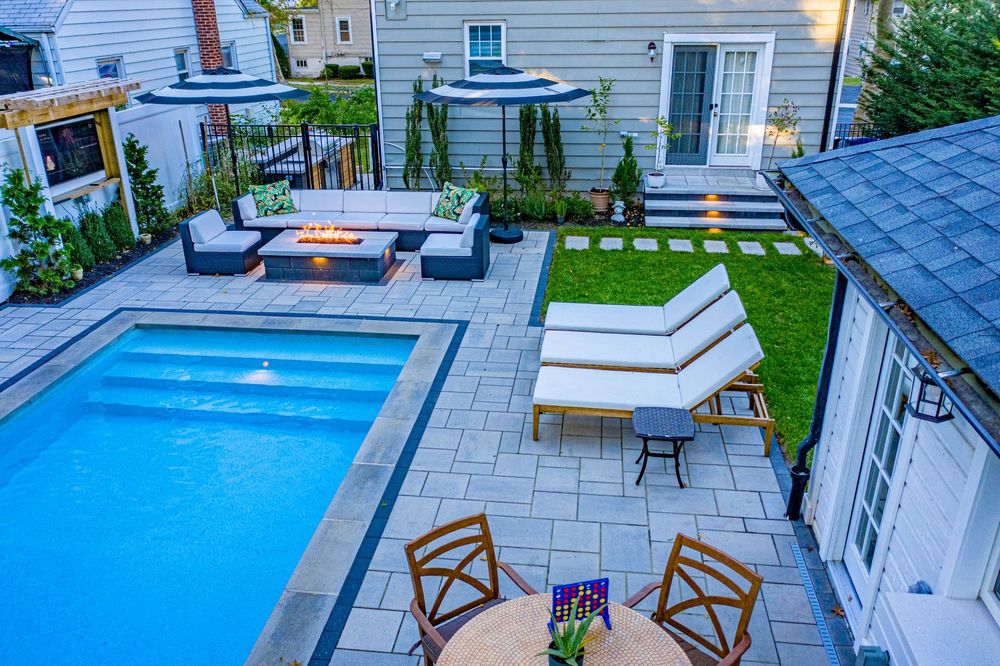 Backyard with pool, patio, and seating area. Features include a fire pit, umbrellas, lounge chairs, and a small dining table.