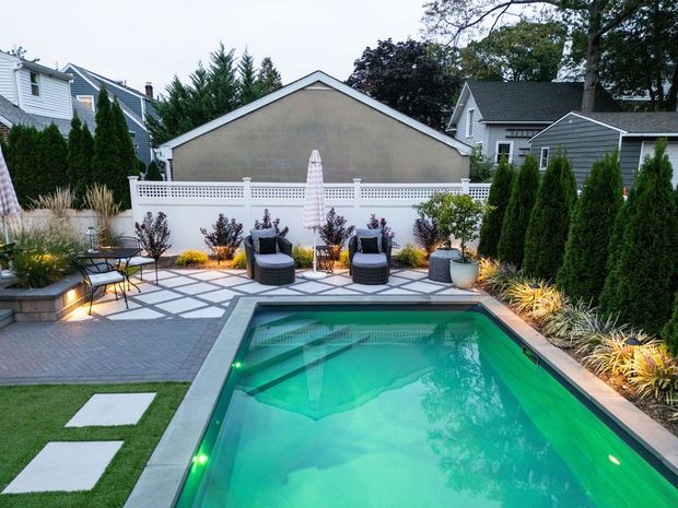 Backyard pool with lounge chairs, trees, and patio in a suburban setting. Green water glows.