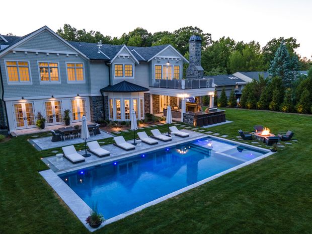 Luxurious home with pool, patio, outdoor kitchen, and fire pit in a lush green backyard at dusk.