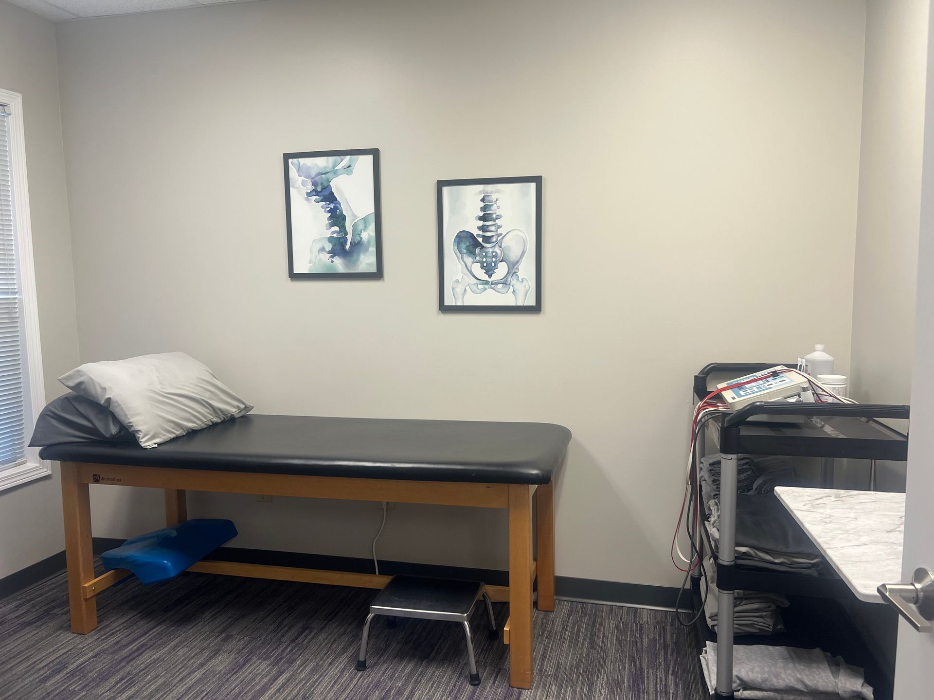 A doctor 's office with a bed and two pictures on the wall.