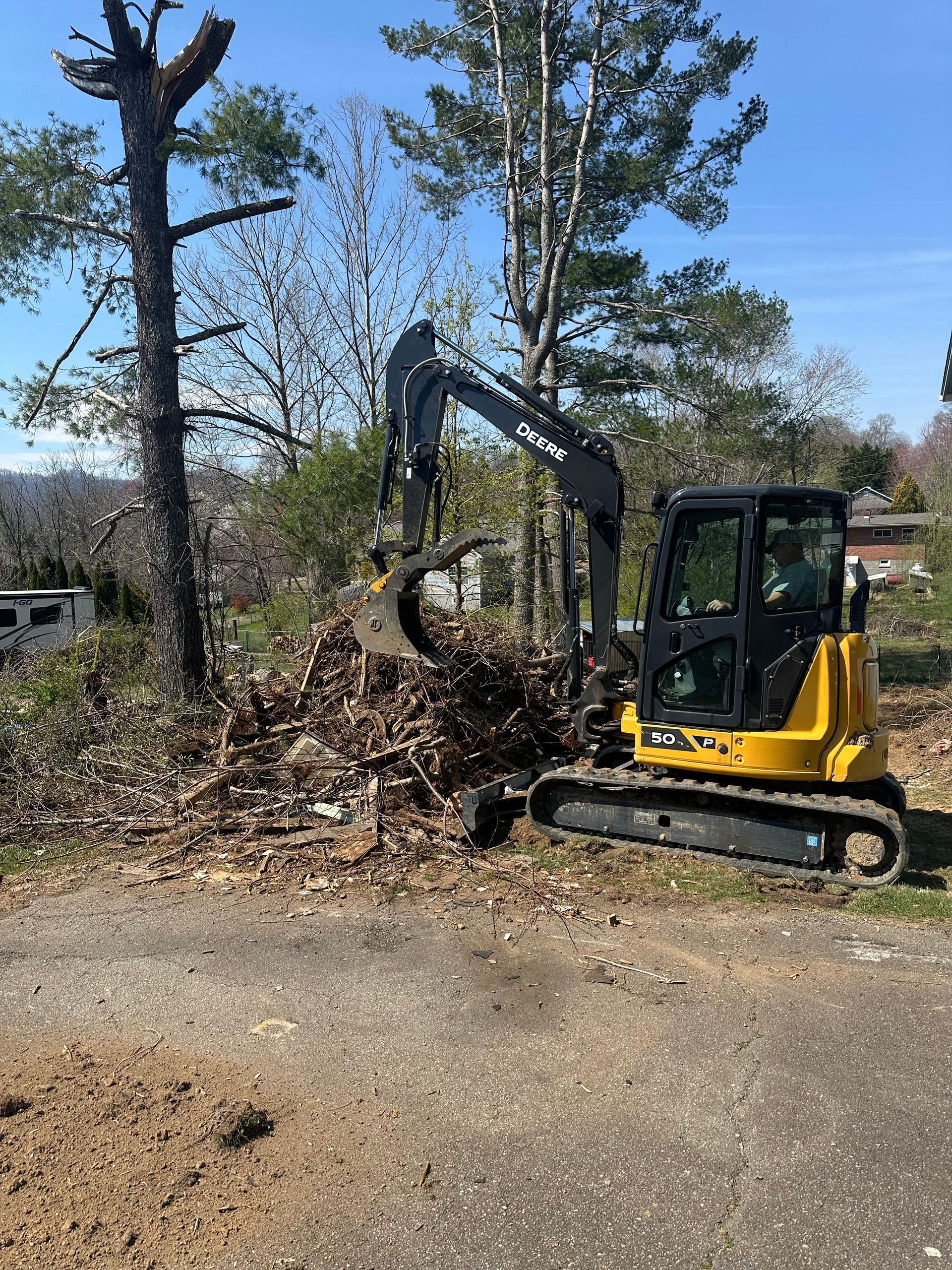 A yellow excavator is moving a pile of dirt next to a tree.