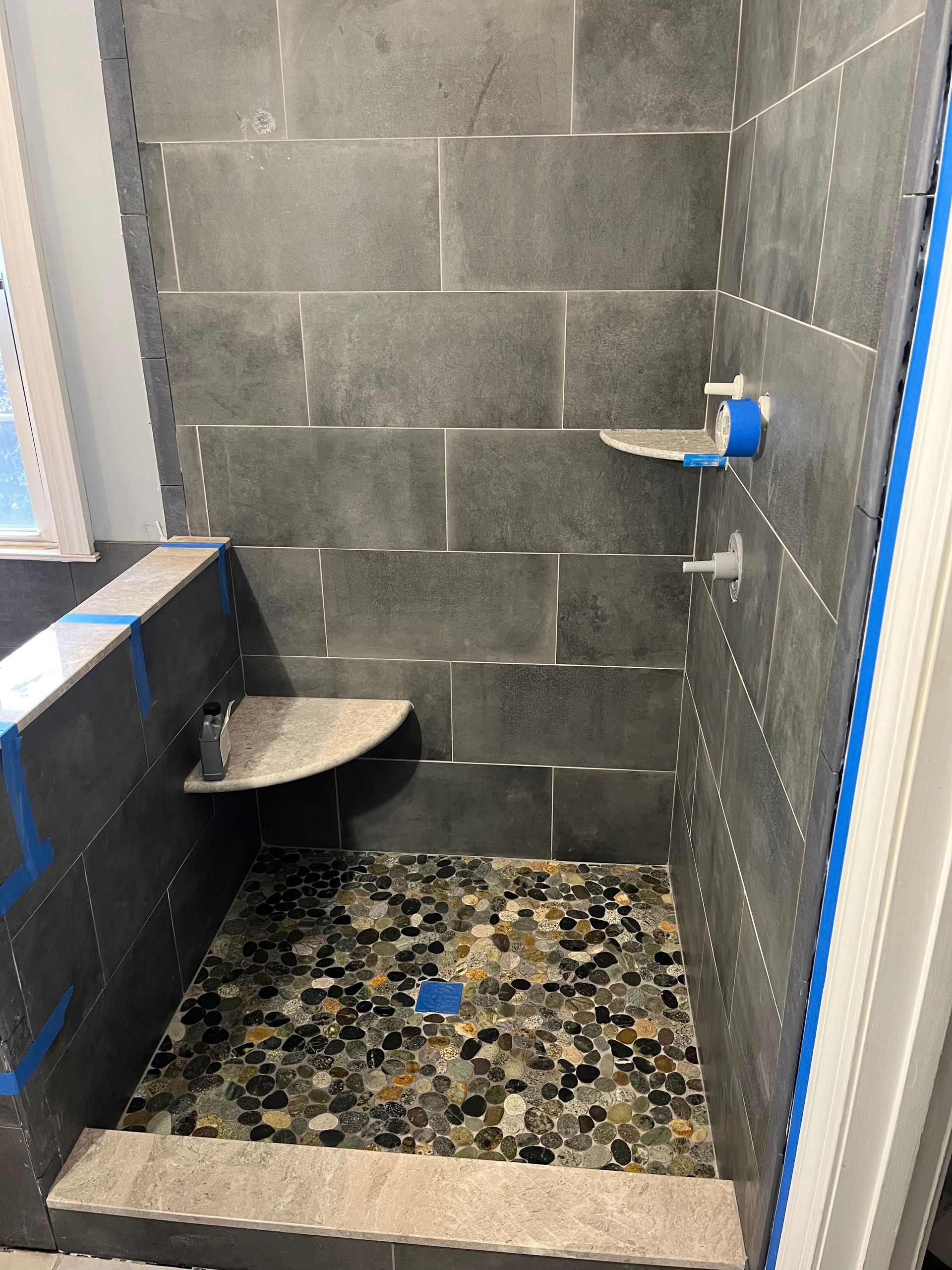 A shower with a tiled floor and shelves is being built in a bathroom.