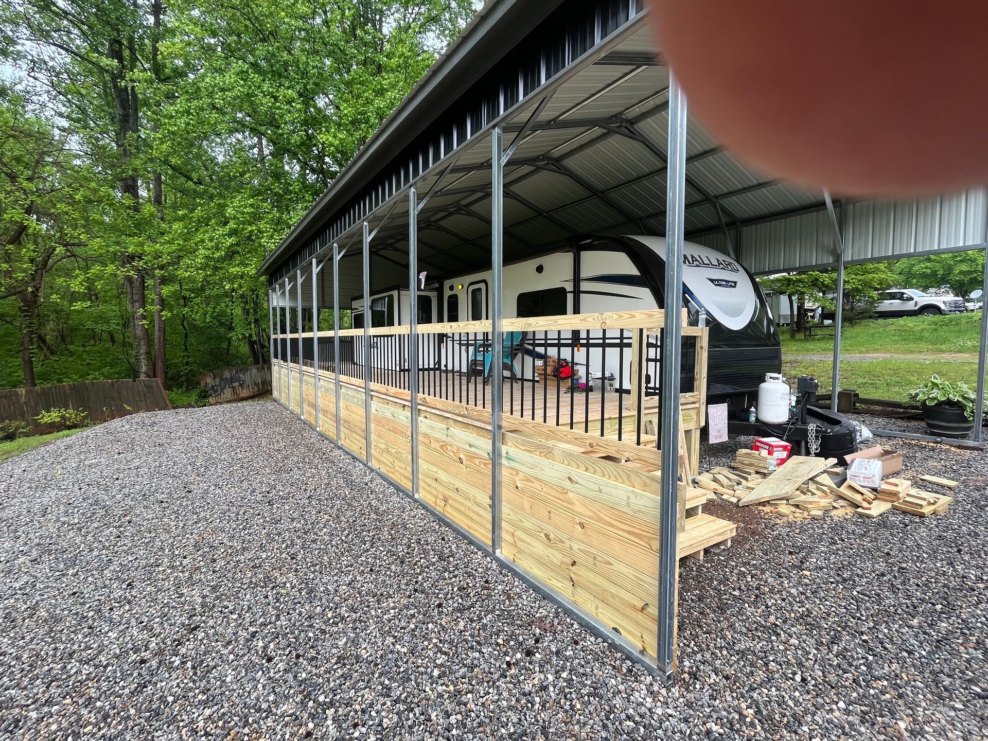 A rv is parked under a metal building with a wooden fence.