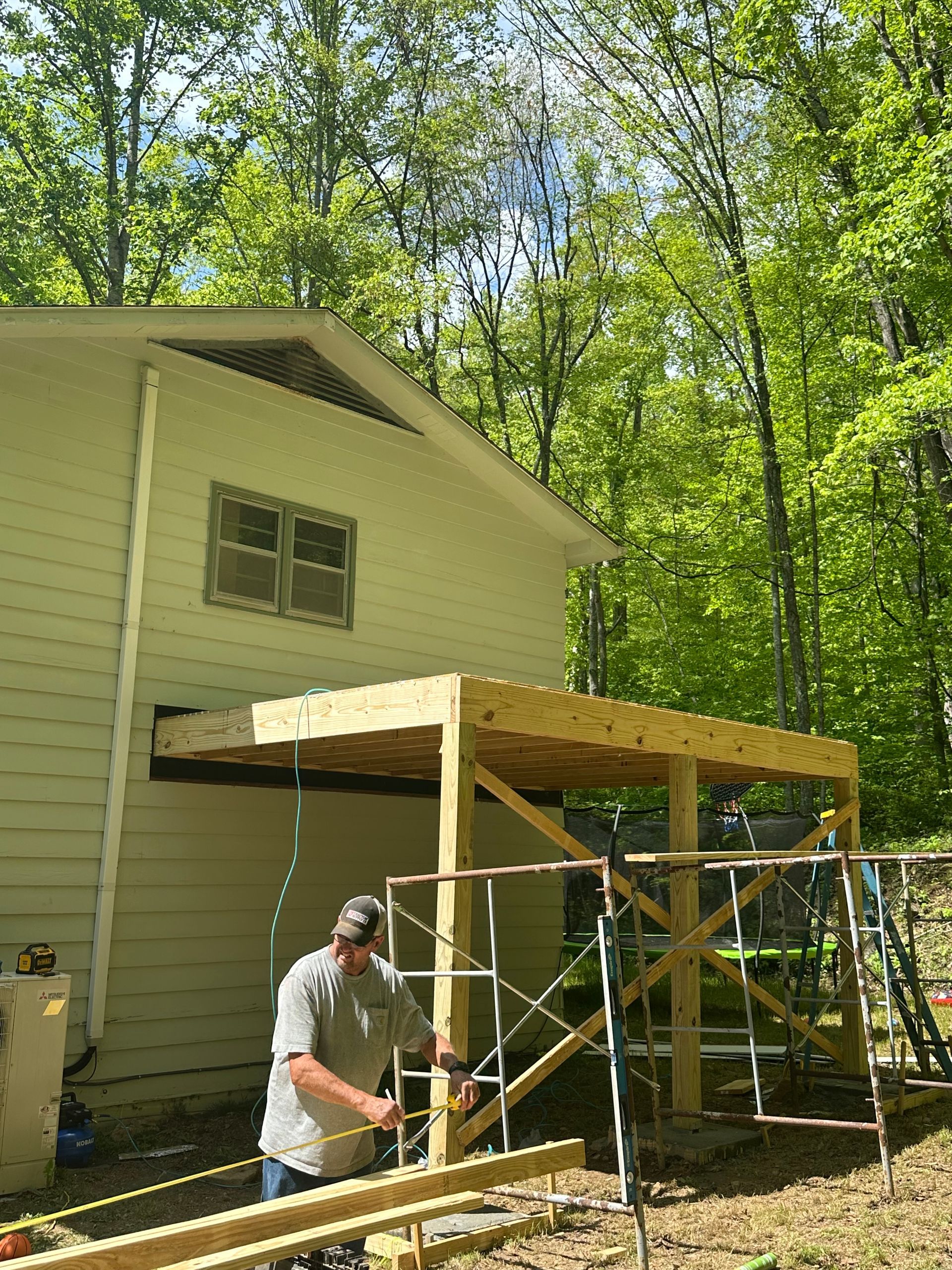 A man is working on a wooden structure in front of a house.