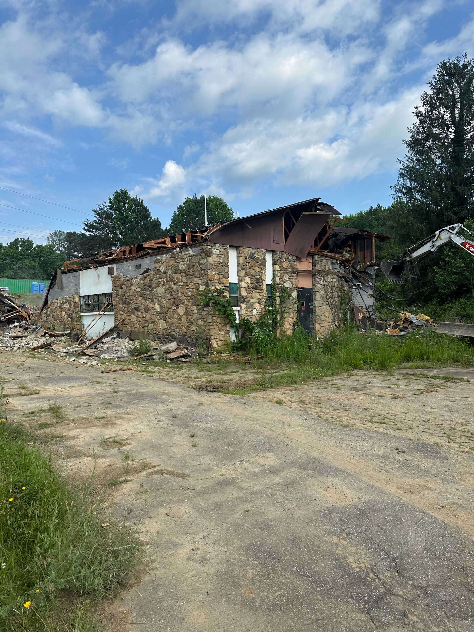A large stone building is being demolished in a dirt field.