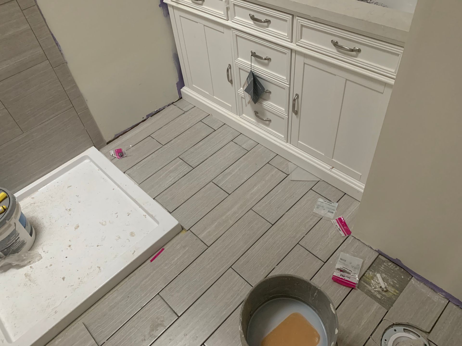 A bathroom with a shower stall and a bowl of paint on the floor.