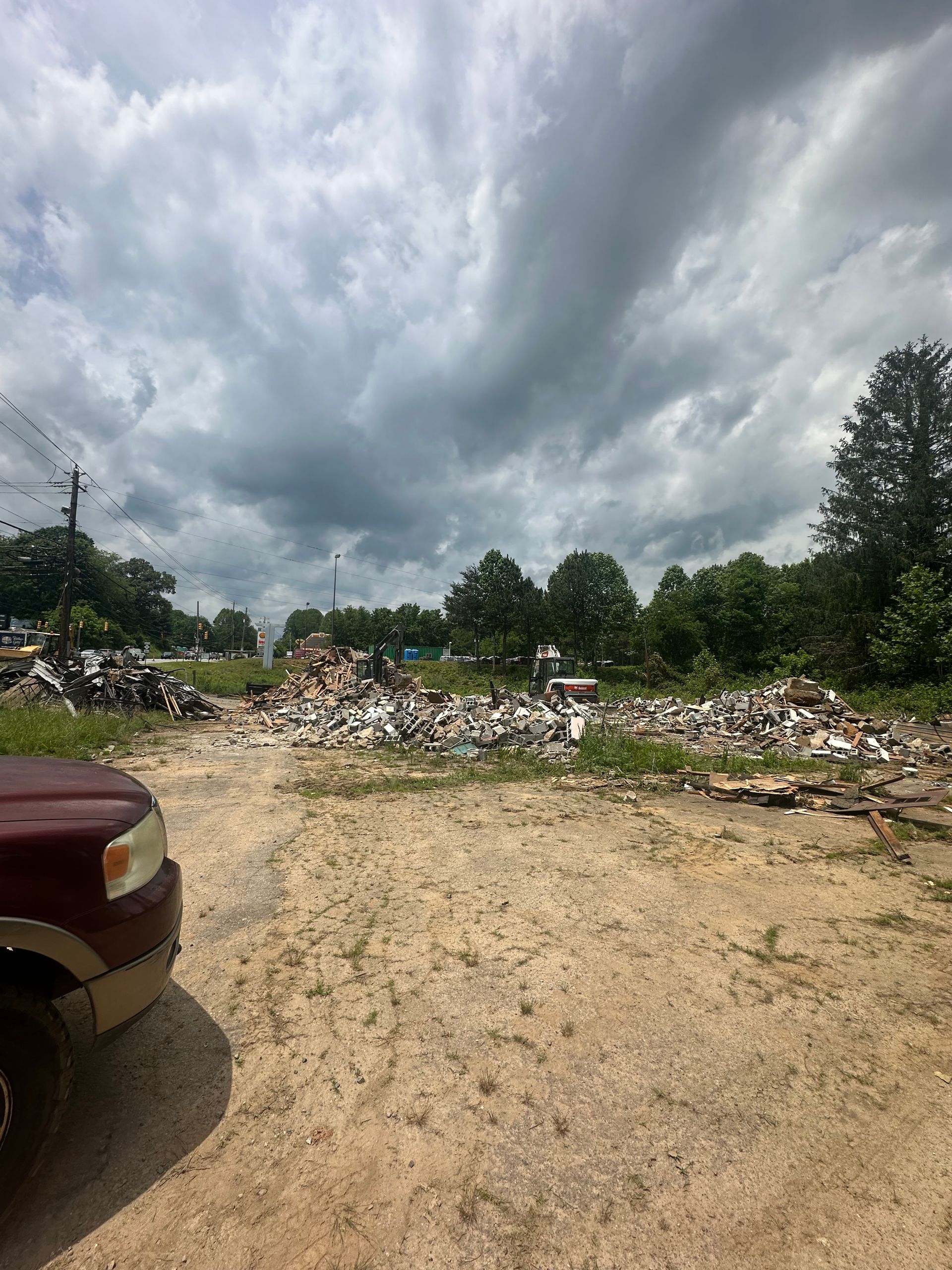 A red car is parked in front of a pile of trash.