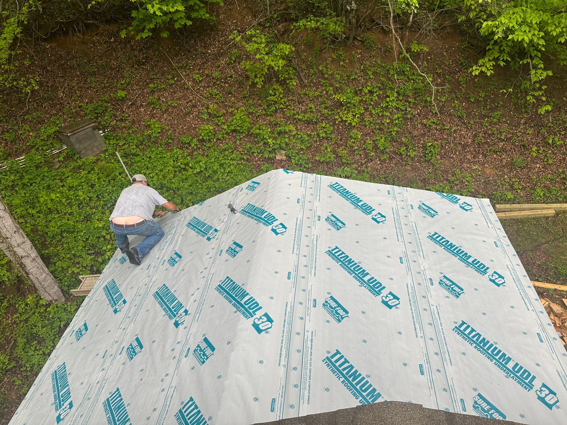 A man is working on a roof with a tarp that says titanium on it.