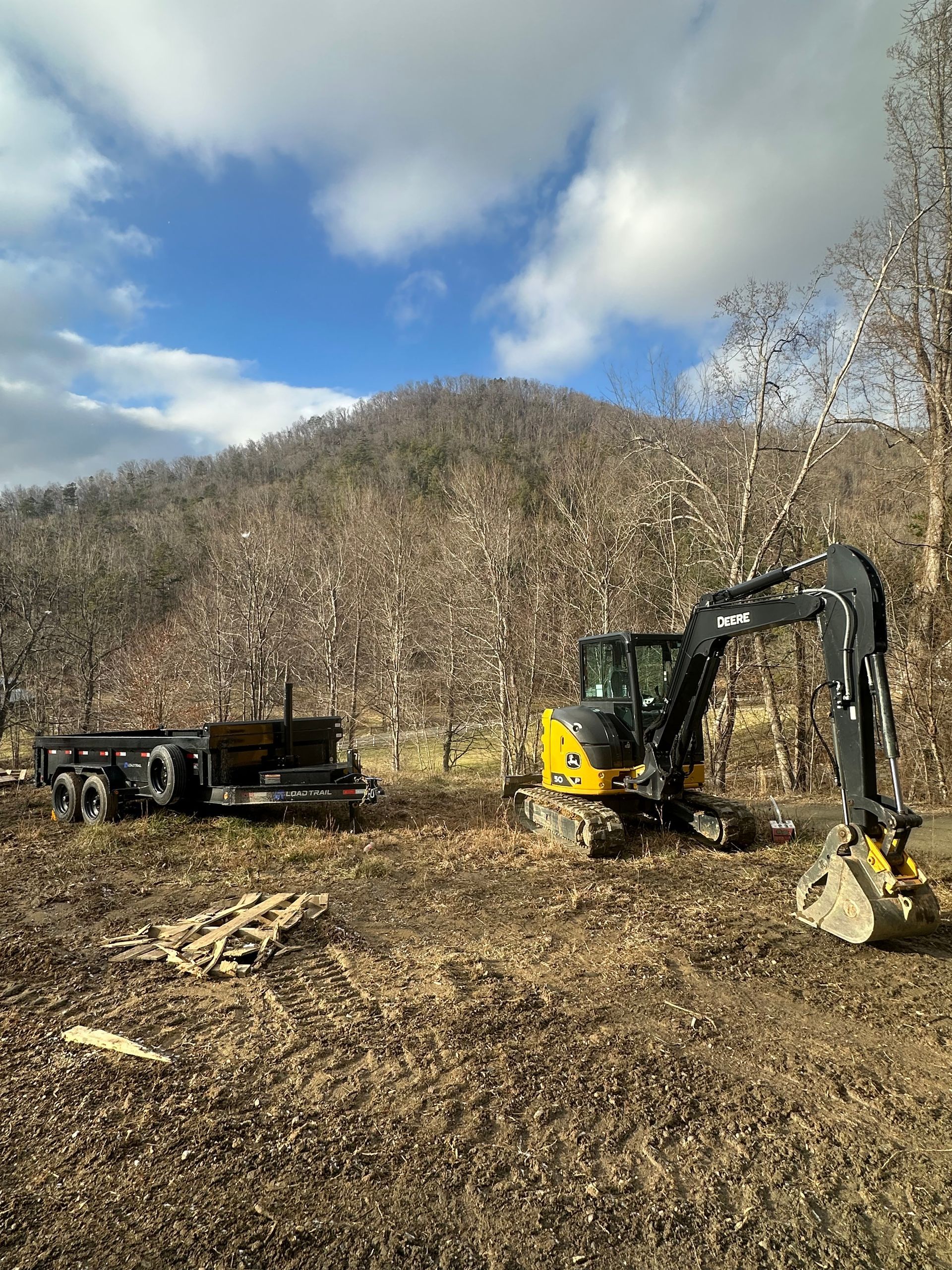 A yellow excavator is sitting in a field next to a trailer.