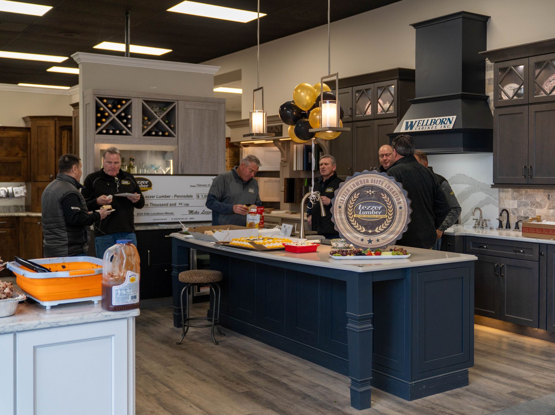 People gathered in a bright kitchen showroom around an island and decorative platter.