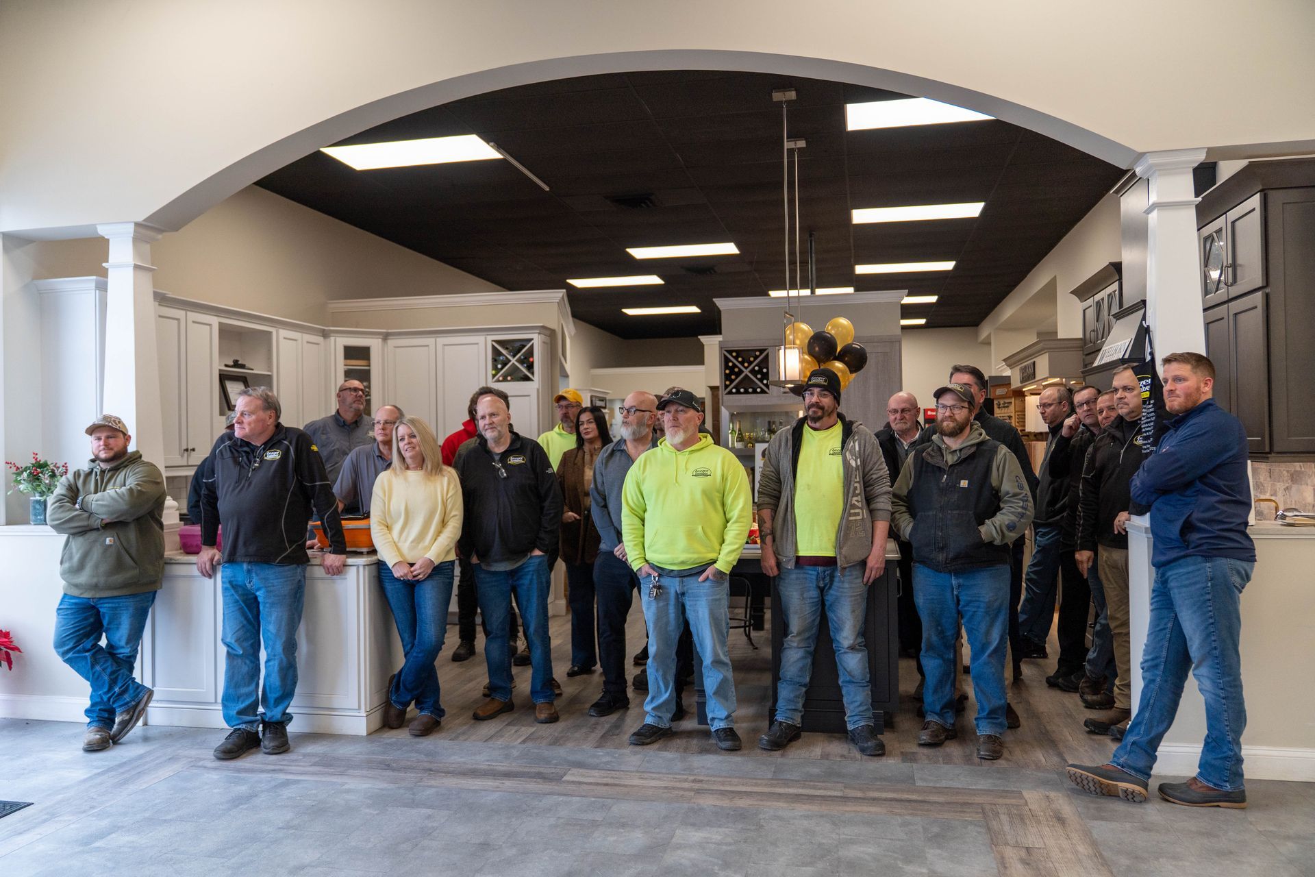 Group of people standing in a lobby beneath a large archway, one person in a neon yellow jacket.