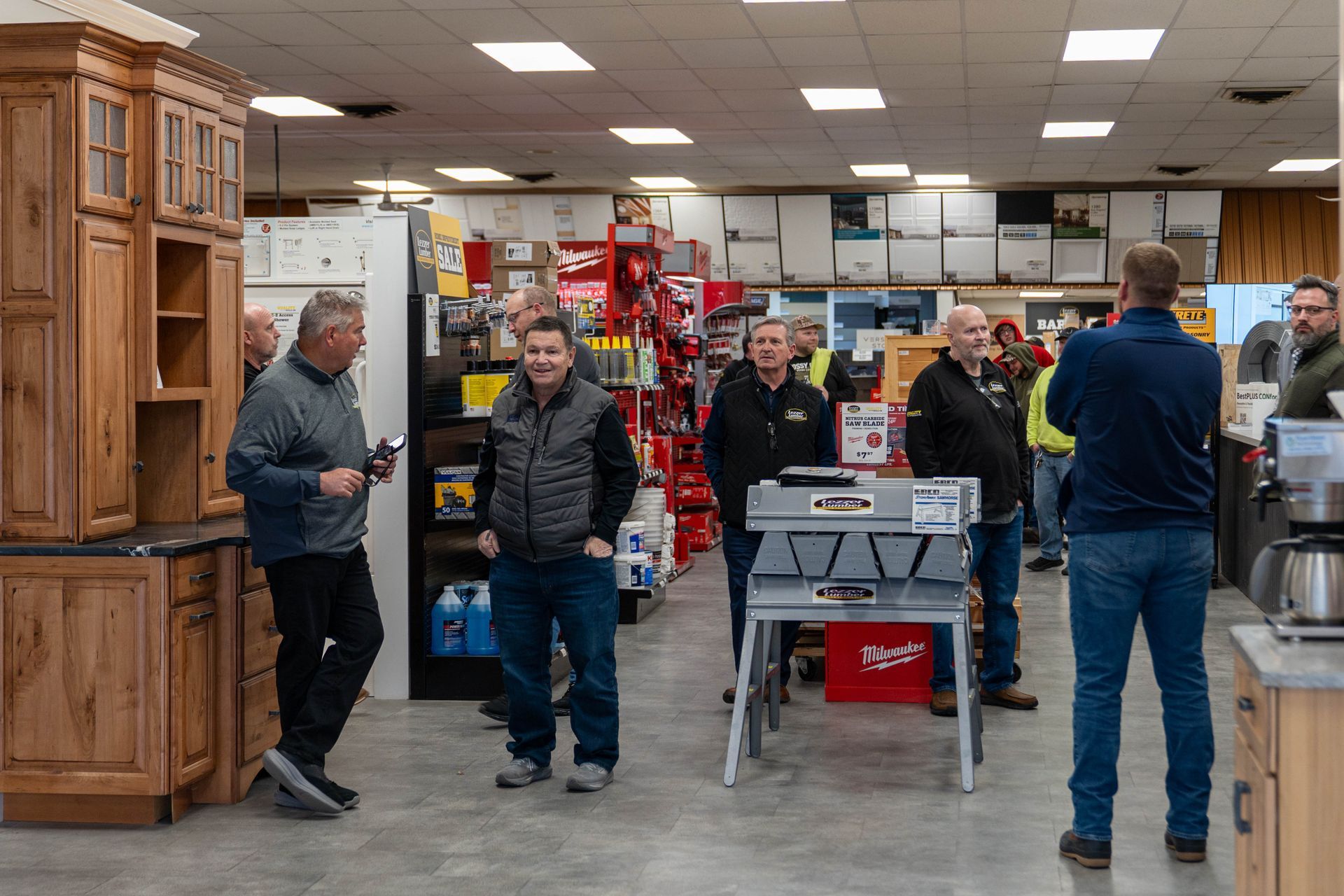 People browsing inside a hardware store, with shelves of tools and a wooden cabinet on the left.