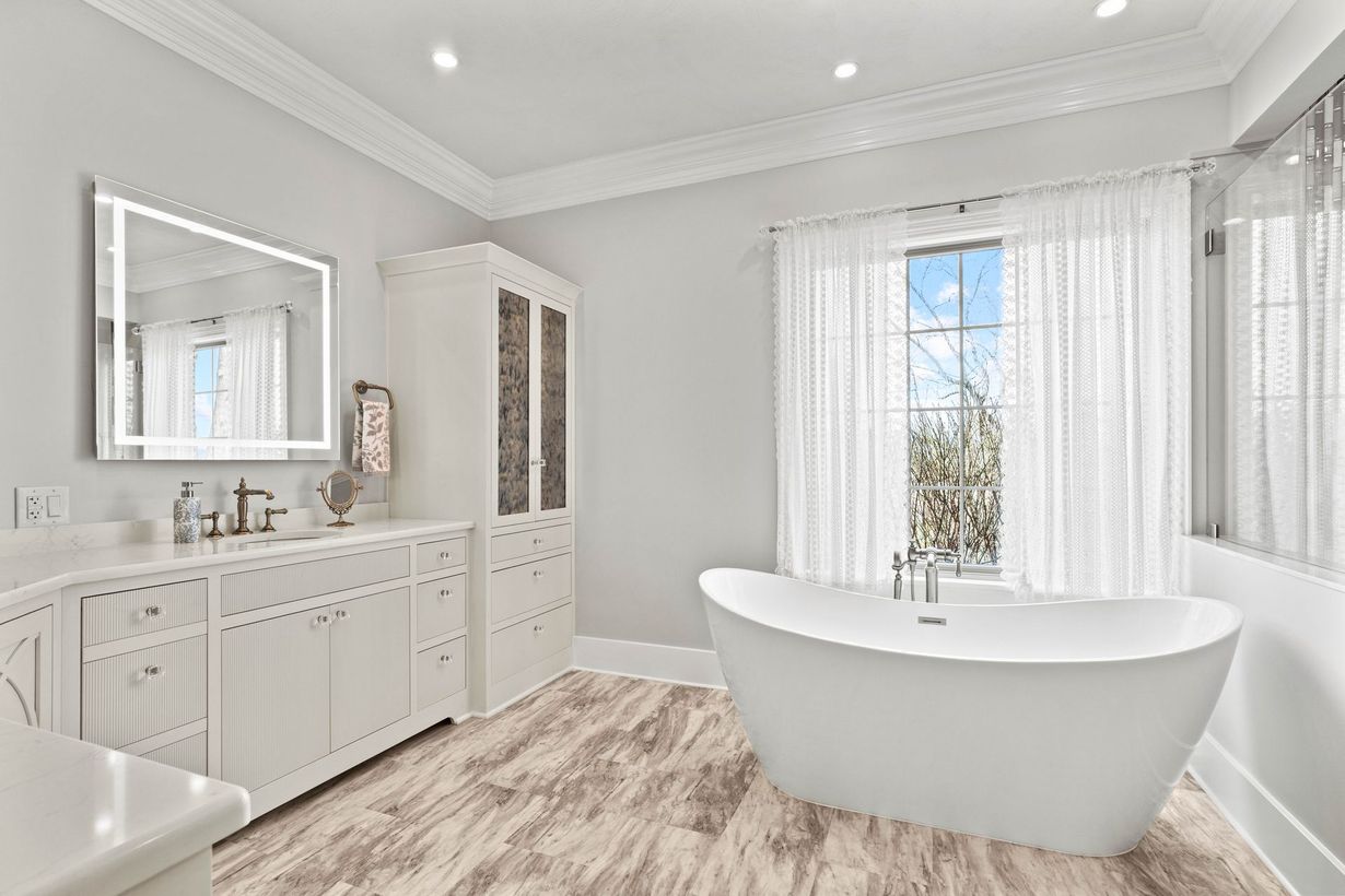 Bright white bathroom with freestanding tub, double vanity, and large window with sheer curtains