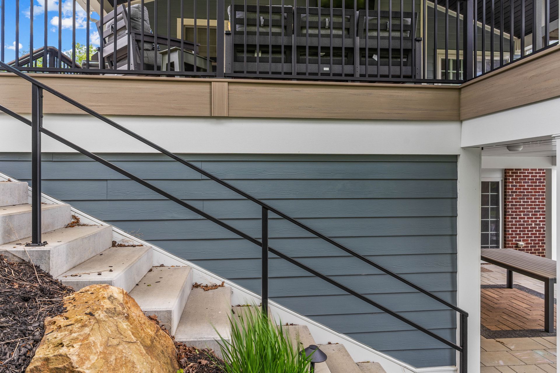 Outdoor staircase with black railing beside a blue-gray house wall and deck
