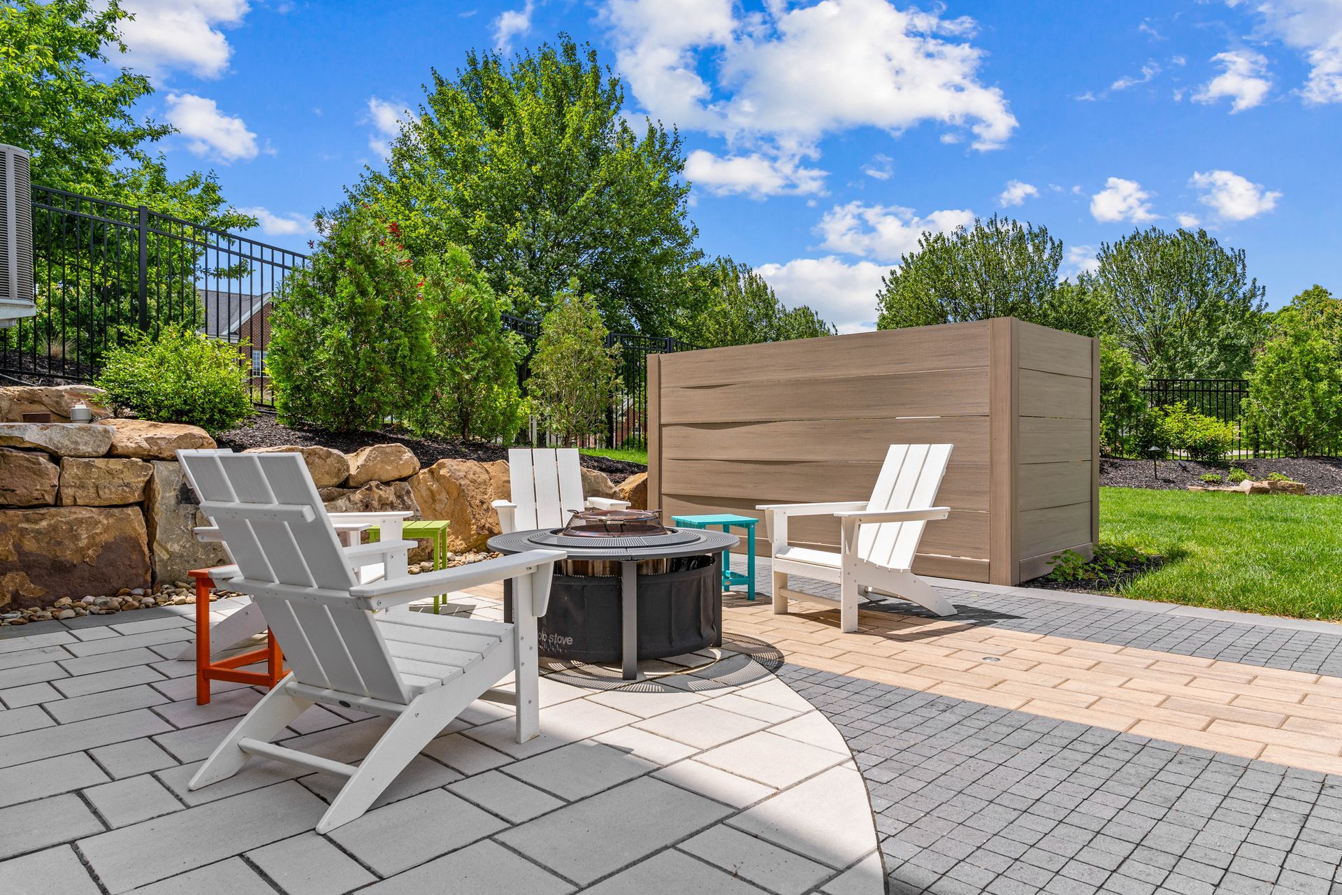 Patio with white chairs, fire pit, and stone seating wall under a blue sky