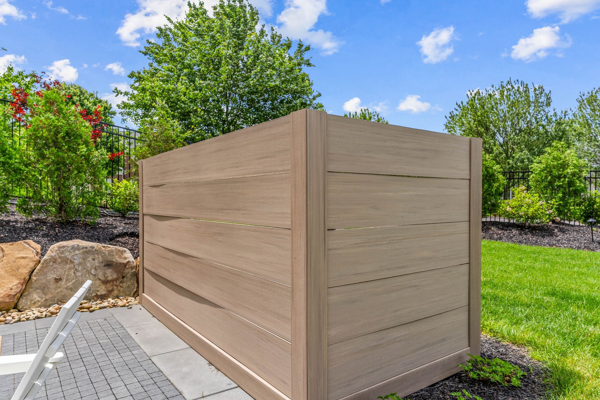 Beige wooden planter box beside a paved path in a sunny landscaped garden with green grass and rocks