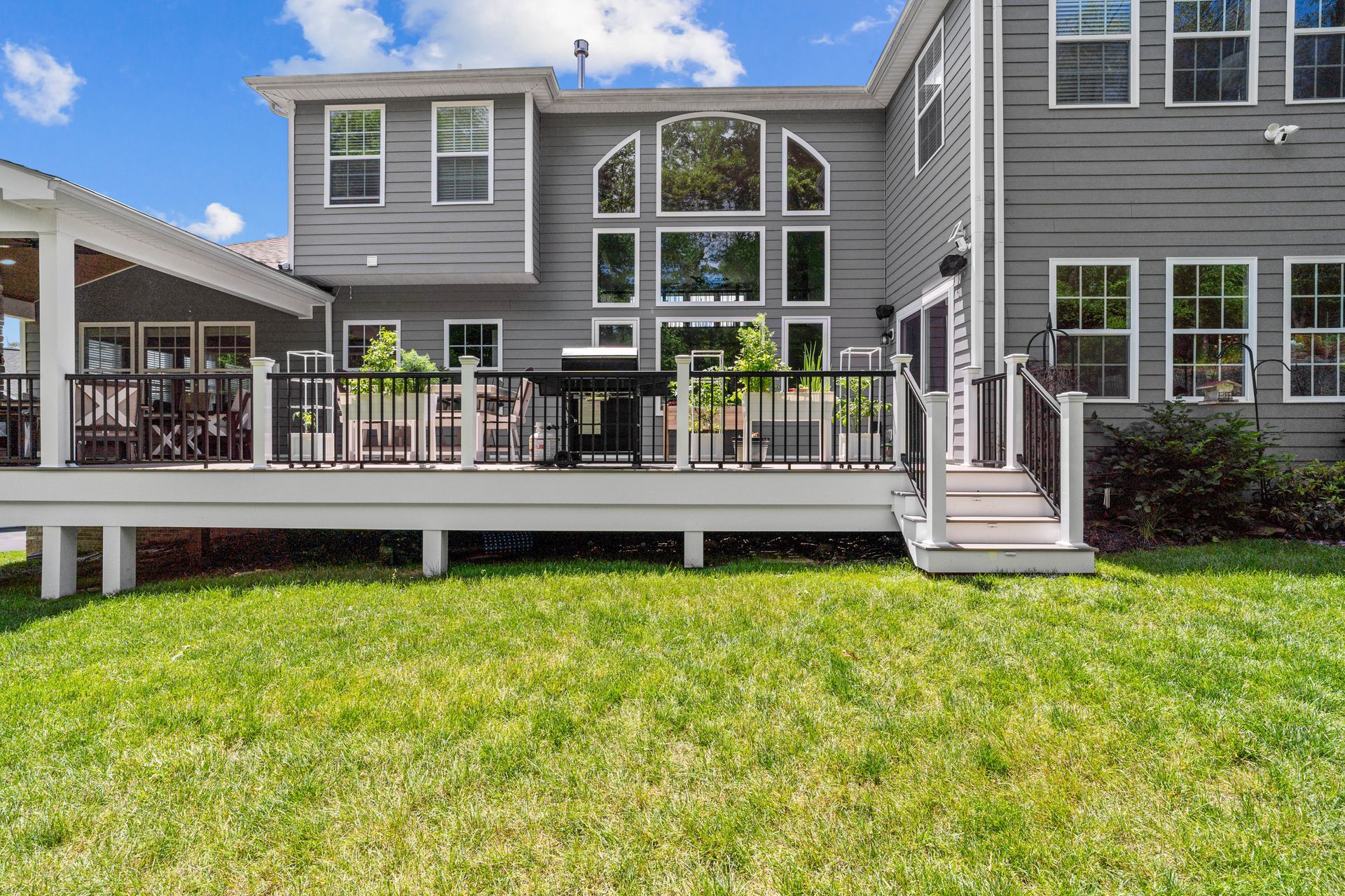 Gray house with raised deck, stairs, and green lawn under a blue sky
