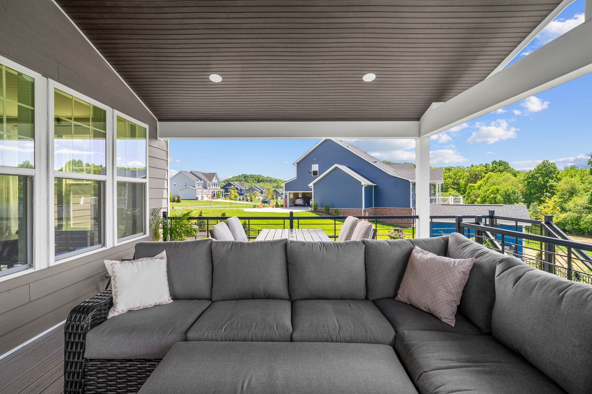 Covered patio with gray sectional sofa, overlooking a bright suburban neighborhood.