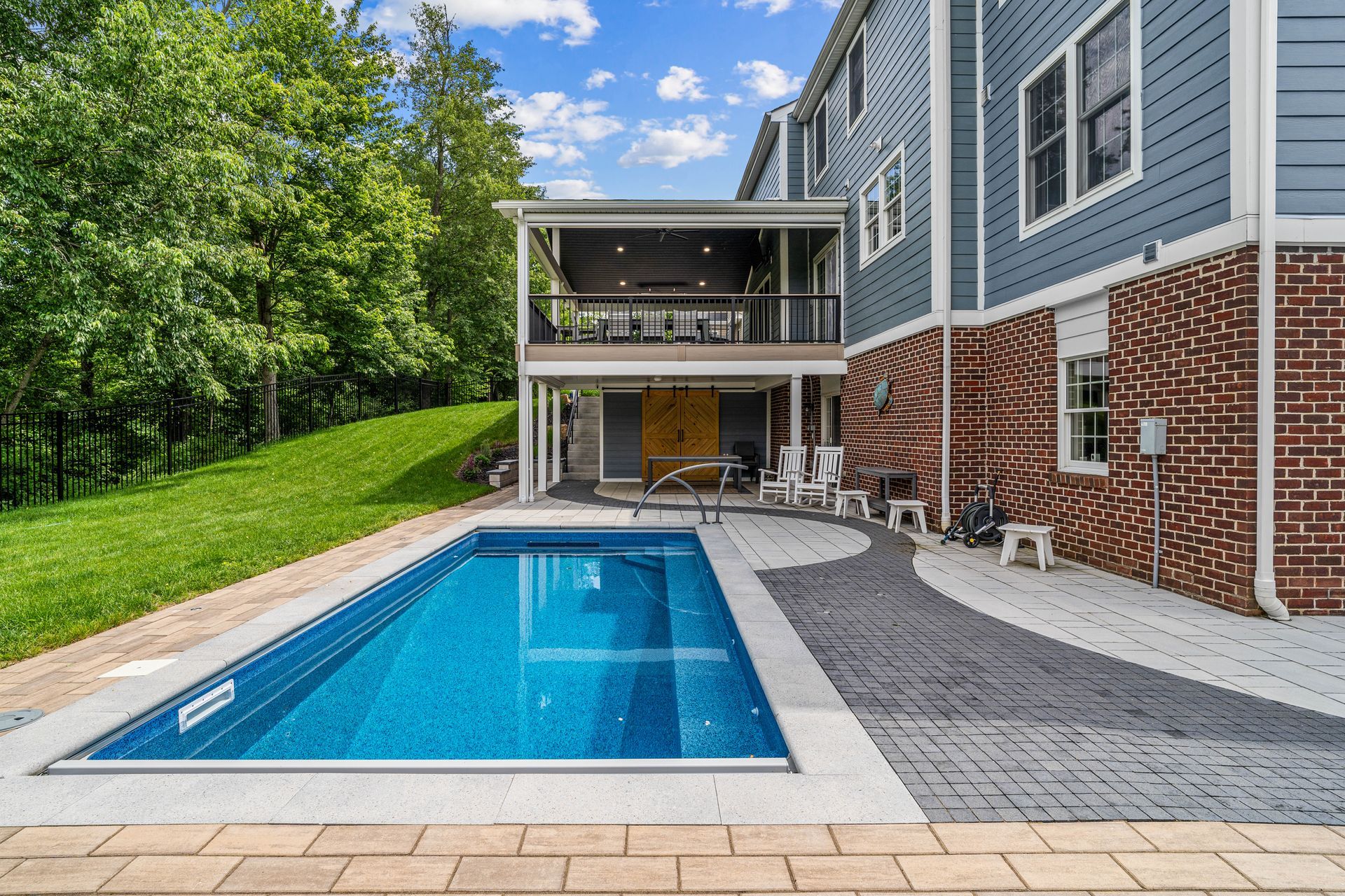 Backyard pool beside a blue-gray house with patio and green trees