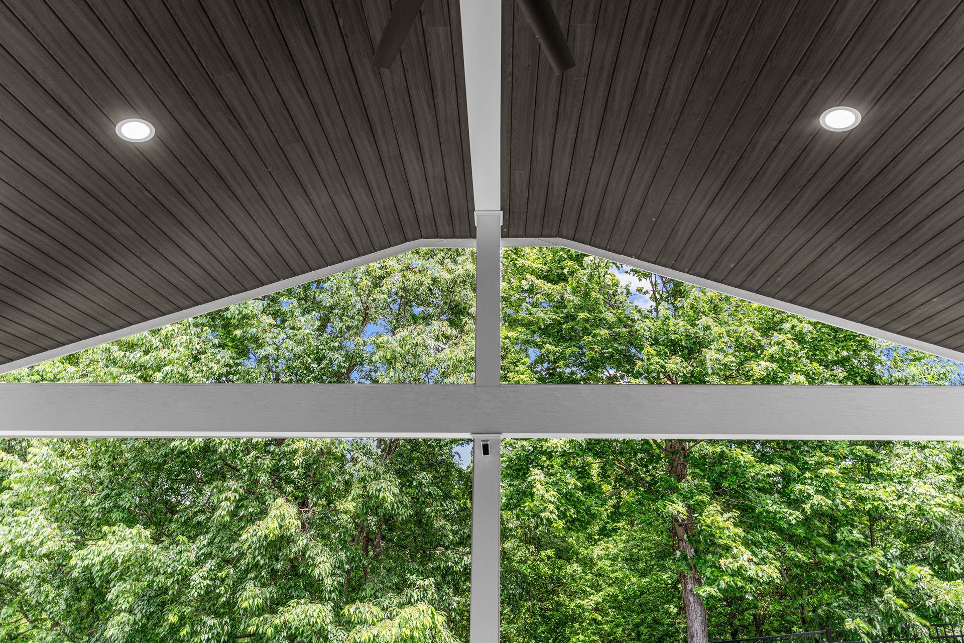 Window view of green trees beneath a slanted ceiling with recessed lights and white beams