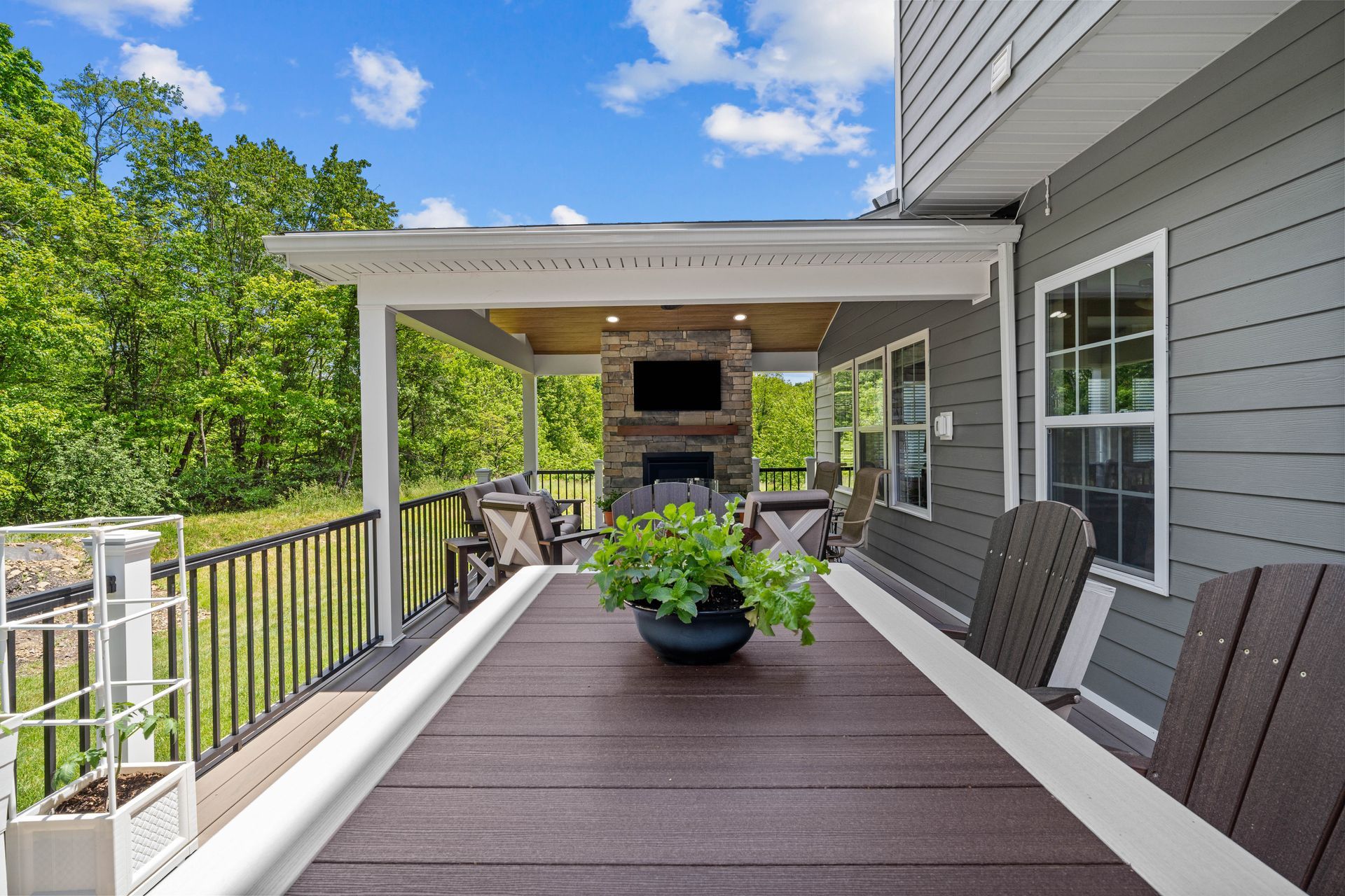 Spacious back deck with dark wood flooring, gray siding, white railings, and a covered patio with potted plants.