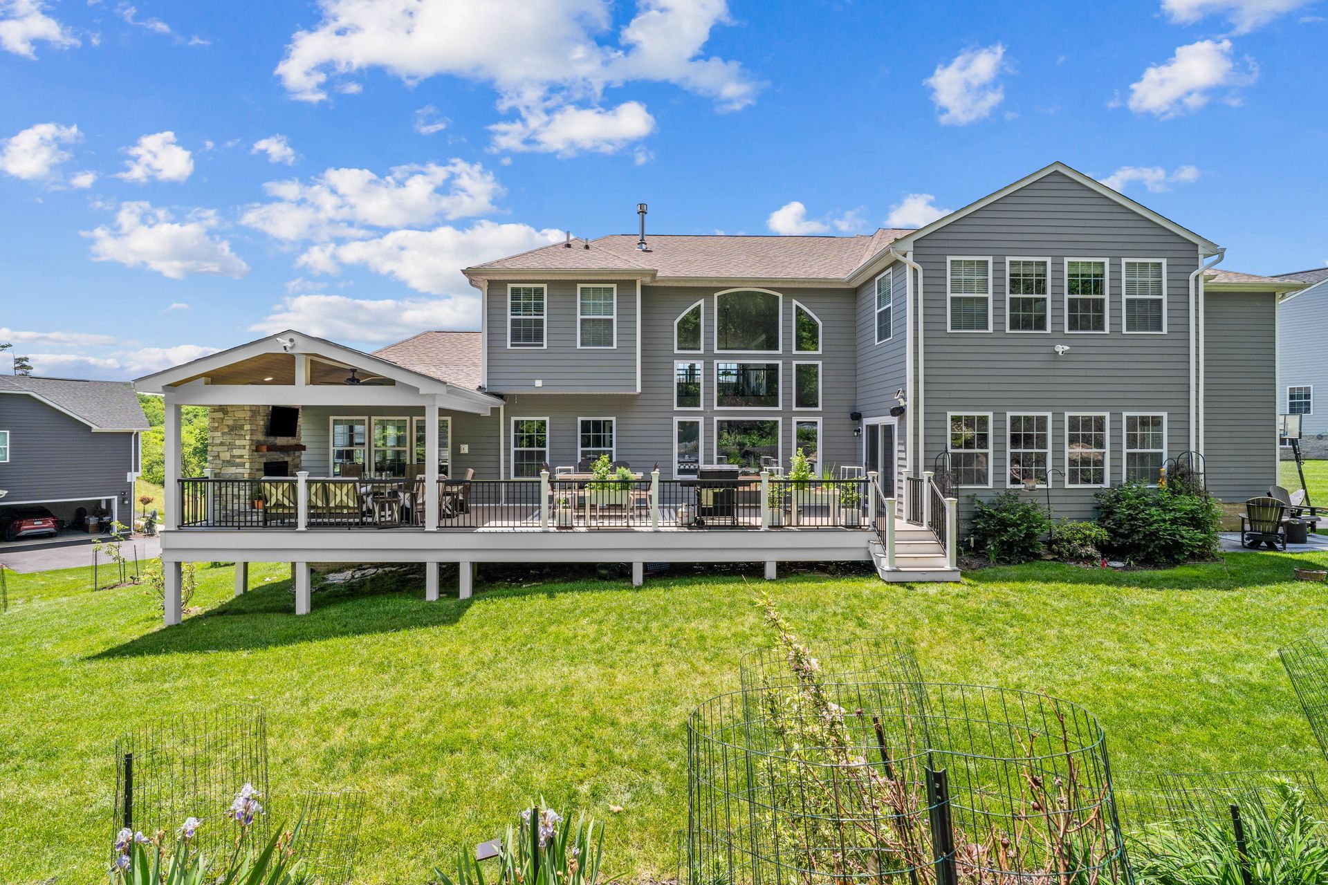 Gray two-story house with a covered deck and large backyard under a blue sky