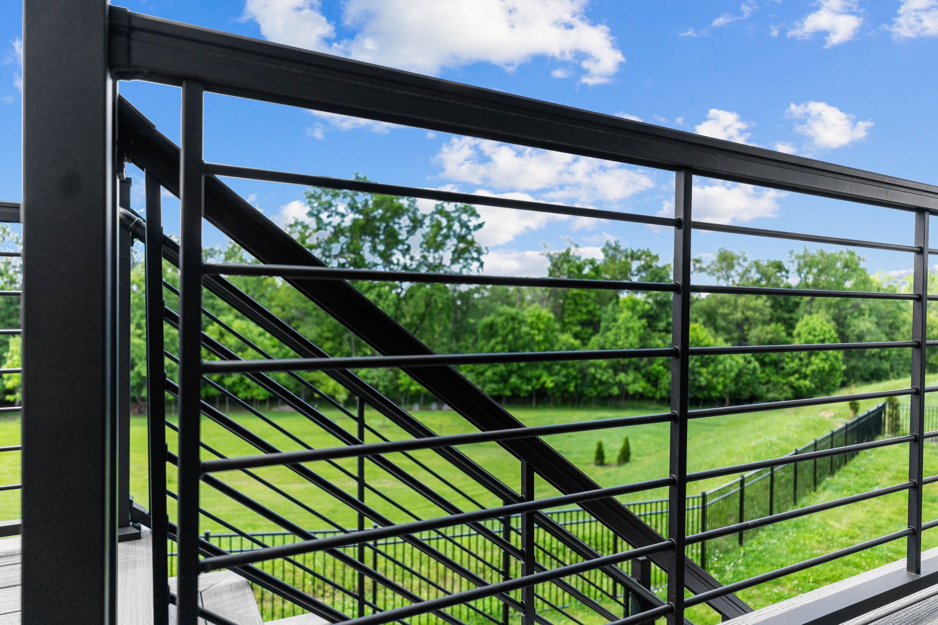Black metal gate with diagonal bars overlooking a green park under a blue sky